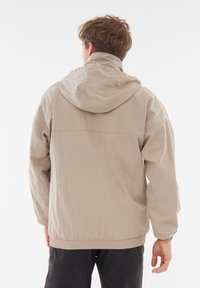 Giacca a vento beige chiaro realizzata in tessuto testurizzato, con una vestibilità comoda, vita elasticizzata e dettagli di cucitura discreti.