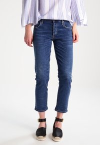 Mörkblå denimjeans med slim fit, kort längd och mindre slitningar; kombinerad med svarta plattform-espadriller.