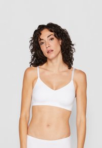 Hvit sømløs bralette med v-hals-design, tynne justerbare stropper og nøytral tone. Myk, glatt stoff med minimale detaljer.