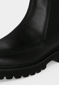 Gros plan d'une botte en cuir noir texturé avec une semelle épaisse à crampons et une couture visible le long du bord.