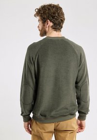 Sweatshirt vert olive avec une finition texturée, manches raglan et patchs au niveau des coudes. Comprend un col et des poignets côtelés, coupe courte.