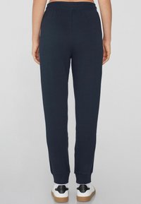 Pantalones de chándal azul marino con un corte relajado, cinturilla elástica y puños ceñidos. Combinados con zapatillas blancas con detalles en negro.