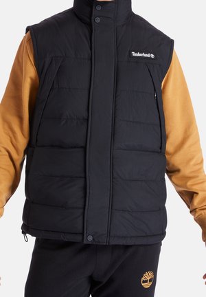 Black puffer vest with a high collar, snap buttons, and side pockets. The vest features a smooth texture and a Timberland logo patch.