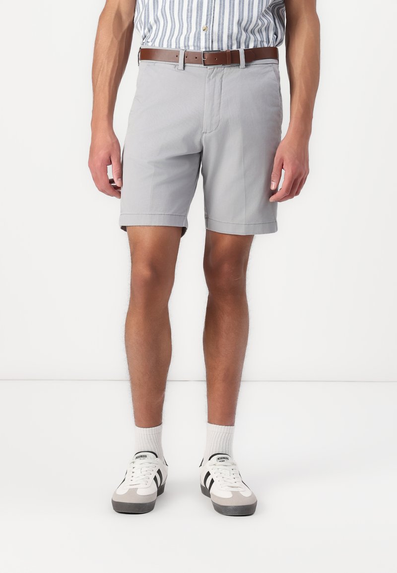 Shorts gris au toucher lisse, avec un ourlet roulé, portés avec une ceinture marron. Associés à une chemise rayée et des baskets décontractées.