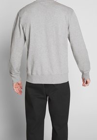Sudadera gris con cuello redondo, puños y cintura acanalados. Detalles de costura visibles y un ajuste holgado. Combinada con pantalones negros.