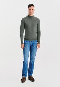 Szary sweter z długim rękawem i kołnierzem typu golf, w połączeniu z niebieskimi dżinsami, uzupełniony brązowymi butami wsuwanymi, o dopasowanym kroju i gładkiej fakturze.