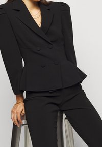 Černý dvouřadý blejzr se strukturovanými rameny, peplum designem a dvěma kulatými knoflíky. Hladká látka v kombinaci s těsně padnoucími kalhotami.