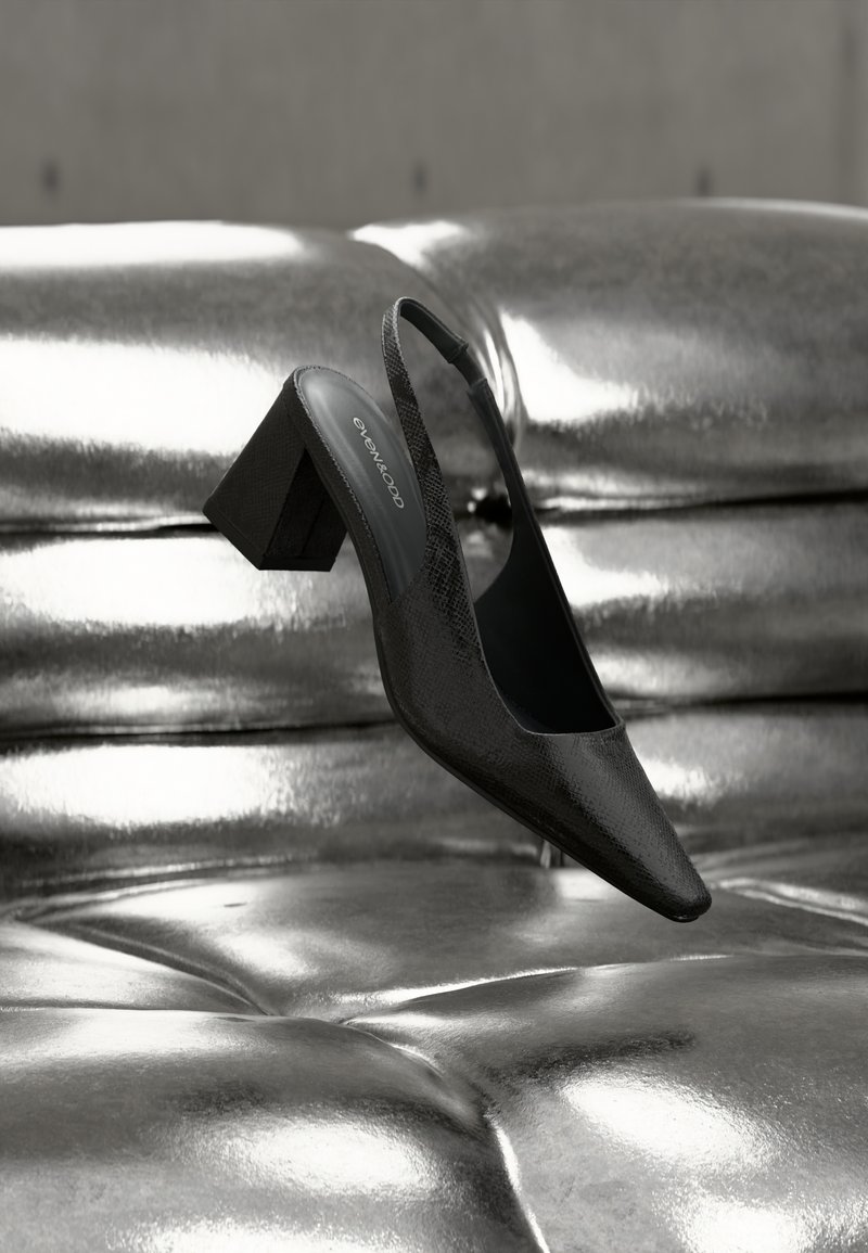 Μαύρο γυναικείο πέδιλο με λουράκι στο πίσω μέρος και μυτερή μύτη, με υφή και χοντρό τακούνι. Τοποθετημένο πάνω σε γυαλιστερό, μεταλλικό φόντο.