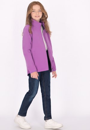 Lilla softshell-jakke med høj krave, frontlynlås og sidelommer, parret med mørke jeans og hvide sneakers. Glat tekstur.