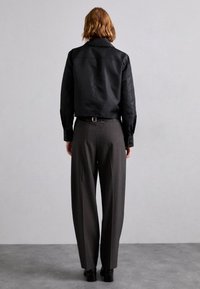 Zwarte cropped jas met knoopmanchetten, gecombineerd met grijze hoog-waist geplooide broeken en chunky zwarte schoenen met hak, gezien van achteren.