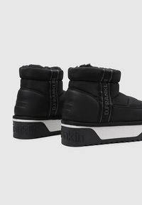 Botas negras hasta el tobillo con un diseño acolchado, textura suave, parte superior alta, suela blanca en contraste y logo de la marca en relieve en la parte posterior.