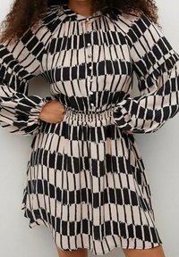 Vestido de patrón negro y beige con mangas abullonadas, cinturilla elástica, botones en la parte delantera y detalle de cuello con ojal. Textura de tela suave.
