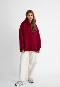 Bordeaux oversized hoodie met een voorzak en een capuchon met trekkoord, gecombineerd met crème wijde broek en grijze sneakers.