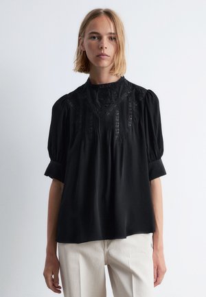 Schwarze Bluse aus weichem Stoff, mit hohem Halsauschnitt, Puffärmeln und aufwendiger Spitze an der Vorderseite und an den Ärmeln.