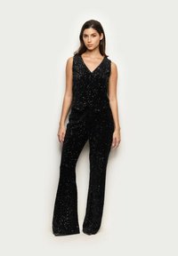 Salopette nera con paillettes, dal collo a V, senza maniche, con pantaloni svasati e una silhouette aderente. La texture scintillante ne esalta l'appeal visivo.