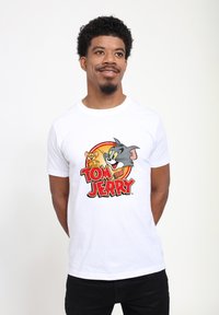 Hvid bomulds T-shirt med en farverig grafik af Tom og Jerry og fed tekst nedenfor, der viser en glat tekstur og klassisk tegnestil.