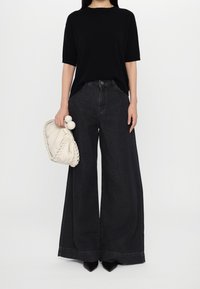 T-shirt noire oversize, jean noir taille haute et jambes larges, sac à main plissé crème avec ferrures décoratives, et escarpins noirs à bouts pointus.