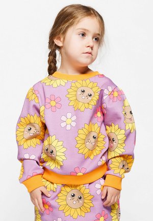 Tröja med lila bakgrund som har gula solrosor med söta ansikten och rosa blommor. Orange ribbstickade ärmslutar och midjeband. Mjuk tyg.
