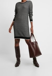 Abito in maglia a strisce bianche e nere con maniche lunghe, scollo rotondo e rifiniture nere; abbinato a una borsa a tracolla in pelle bordeaux e stivali al ginocchio.