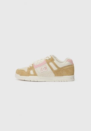 DC skate sko med en beige ruskinds- og creme tekstiloverdel, lyserøde accenter, perforerede detaljer og en hvid gummisål.