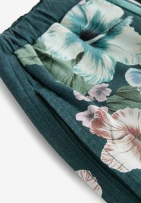 Kukakanka, joka esittää ylisuurta hibiskuskuviota teal- ja vaaleanpunaisissa väreissä tummanvihreällä taustalla, pehmeällä ja tekstuurilla viimeistelyllä.