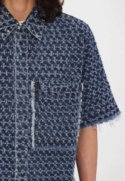 Denim shirt in dark blue with textured weave, short sleeves, a chest pocket, and frayed details along the edges and seams.