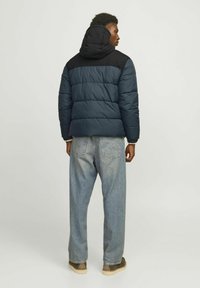 Blue and black padded jacket with a hood, featuring horizontal stitching, worn with light blue jeans and beige shoes. Visible back details.