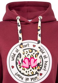 Bordowa bluza z kapturem z wciąganym sznurkiem w leoparda, dużym okrągłym nadrukiem z sercami i napisem "dziki w sercu". Miękka tekstura tkaniny.