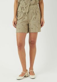 Khaki shorts med broderte blomsterutsnitt, elastisk midje og sydd kant. Kombinert med hvite blokkhevede sko.