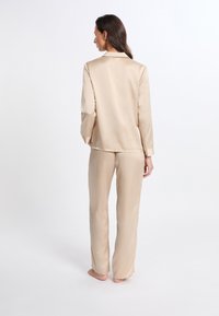 Beige Satin-Pyjama-Set mit einem Langarm-Oberteil mit Kragen und passenden, gerade geschnittenen Hosen. Weicher Stoff und minimales Design.