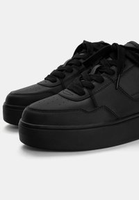 Czarne sneakersy z teksturowaną skórzaną cholewką, płaskimi sznurowadłami, perforowanym przodem oraz grubą czarną gumową podeszwą.