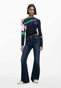 Mörkblå långärmad topp med färgglada blommönster, kombinerad med mörkblåa utsvängda jeans. Outfitten kompletteras med ljusa sneakers.