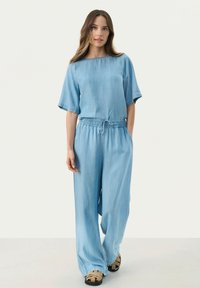 Ljust blå denim tvådelat set med en kortärmad topp med rund hals och lösa, vida byxor med resårmidja.