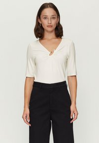 Witte short-sleeve top met een V-hals en een decoratieve twist in het midden, gecombineerd met zwarte high-waisted broek. Eerlijke textuur, schoon ontwerp.