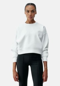 Sweatshirt en coton mélangé blanc avec un col rond, des épaules tombantes et une inscription en relief subtile. Associé à un legging noir avec des détails de couture.