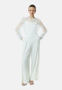 Weiße, mit Blumenstickerei verzierte, transparente Bluse mit Puffärmeln, kombiniert mit hochtaillierten, weit geschnittenen weißen Hosen; glatte Textur, taillierte Passform.