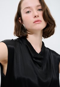 Top in satin nero con scollo a cowl e design senza maniche, caratterizzato da una texture liscia e dettagli di cucitura minimi.