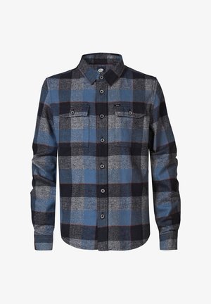 Camisa de franela en cuadros azules, negros y grises con dos bolsillos en el pecho; combinada con jeans grises de corte slim y zapatillas en blanco y negro.