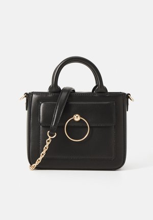 Bolso de piel negra con un diseño estructurado, asas superiores, una correa de cadena desmontable y un acento de hardware circular dorado en la parte frontal.