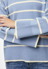 Ljusblå stickad tröja med vita horisontella ränder, med ribbade ärmslut och nederkant. Mjuk textur och avslappnad passform.