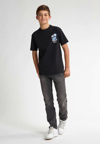 Musta puuvillainen T-paita, jossa sininen kuvio rinnassa, yhdistetty tummanharmaisiin farkkuihin ja valkoisiin tennareihin, luoden rentoon tyyliin.