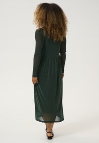 Long green dress with long sleeves, made of shimmery material; fitted bodice with a waist seam and flowing skirt; transparent texture at sleeves.