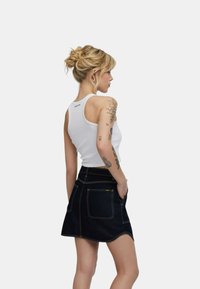 Top in cotone bianco senza maniche con scollatura rotonda, abbinato a una mini gonna di jeans scuri con cuciture gialle e tasche.