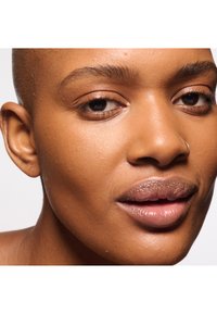 Primer plano del rostro de una persona con piel suave y de tono uniforme, un color sutil en los labios, cejas naturales y un pequeño aro plateado como pendiente.