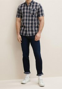 Korte mouwen geruit overhemd in marineblauw, rood en wit, met een button-down kraag en een enkele borstzak, gecombineerd met donkere jeans en witte sneakers.