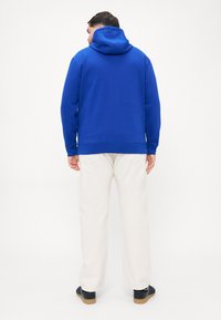 Blauwe sweatshirt met een capuchon, met een soepele textuur en geribbelde manchetten. Gepaard met lichtgekleurde broeken en zwarte instapschoenen.