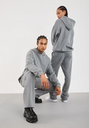 Grey hoodie and sweatpants set made of soft fabric, featuring loose fit, ribbed cuffs, and contrasting sneakers in black and white.