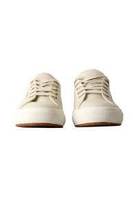 Zapatillas de goma beige con una puntera texturizada, que presentan cordones planos y una suela de goma marrón. Diseño minimalista con marca visible.