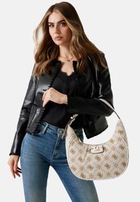 Sac hobo beige avec un motif en relief marron et des détails en or. Texture lisse, forme courbée et une poignée structurée.