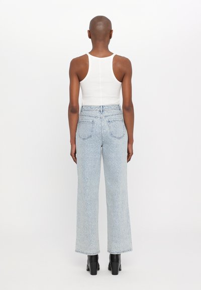 Hellblaue High-Waist-Jeans mit weitem Schnitt, featuring Gesäßtaschen und einem rohen Saum. Kombiniert mit einem weißen ärmellosen Top.